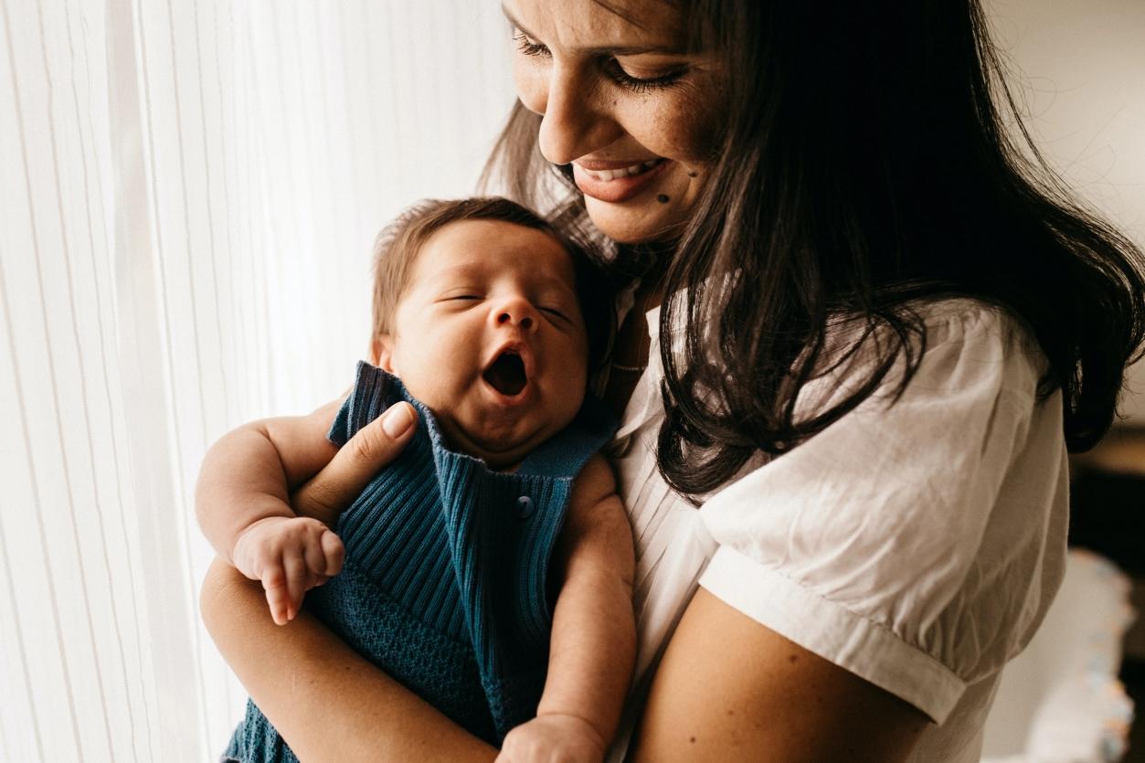 Une mère souriante avec son bébé dans les bras qui baille